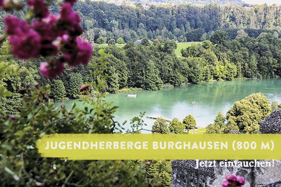 Blick über den Wöhrsee. Das Foto wird überlagert von dem Schriftzug "Jugendherberge Burghausen - jetzt eintauchen".
