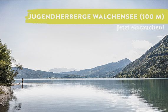 Blick über den Walchensee, der von Bergen umrahmt ist. Dem Foto überlagert ist der Schriftzug "Jugendherberge Walchensee - jetzt eintauchen".