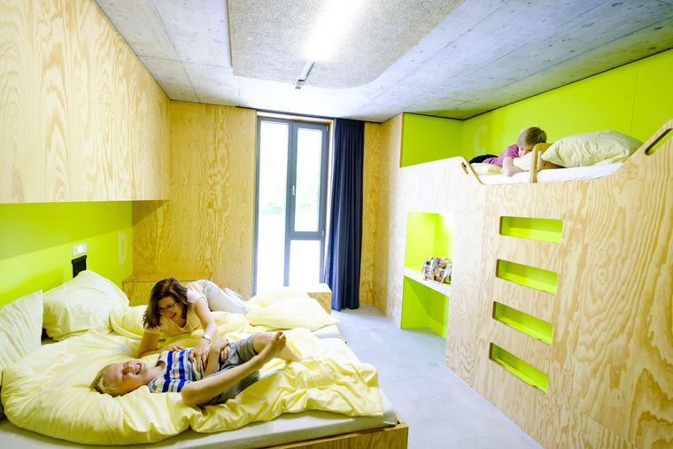 Ein helles Zimmer mit hellgrünen Wänden in der Jugendherberge Bayreuth, in der eine Mutter mit zwei Kindern herumtobt