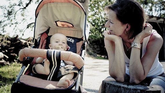 Eine Mutter sitzt neben einem Kinderwagen, in dem ein fröhliches Baby liegt.