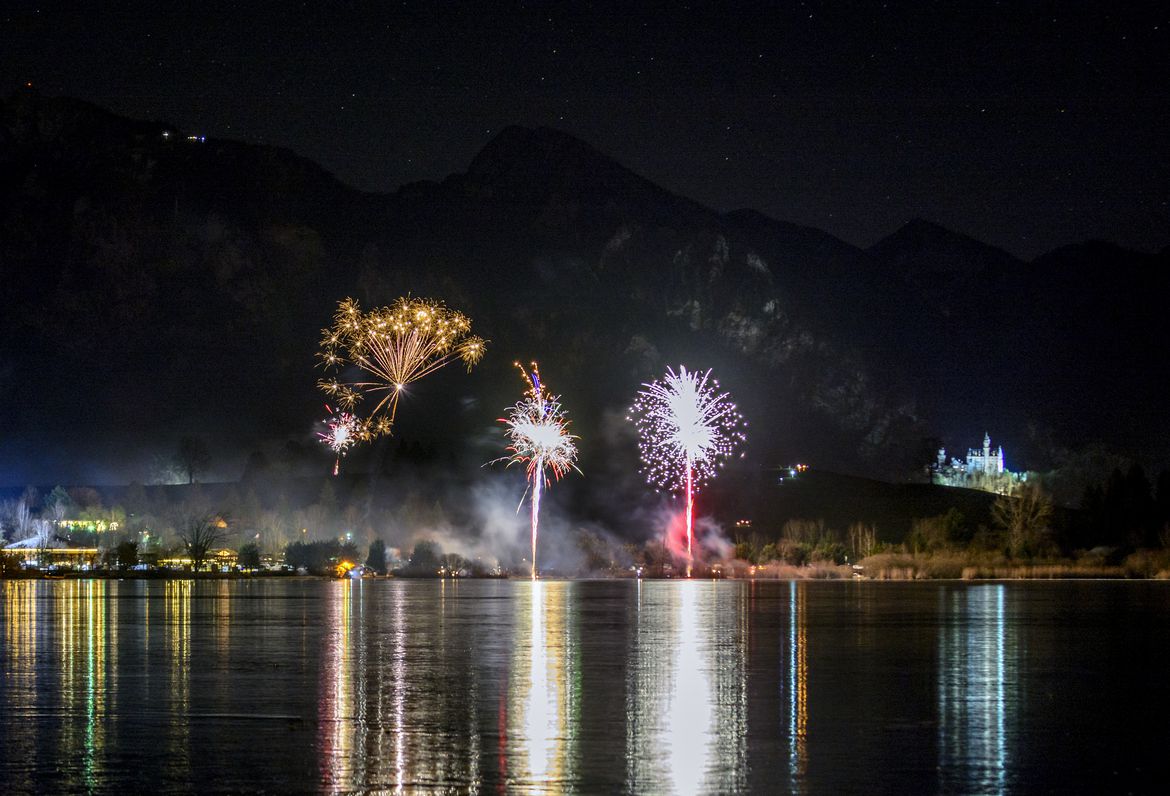 Ein buntes Feuerwerk über einem See mit Spiegelungen im Wasser.