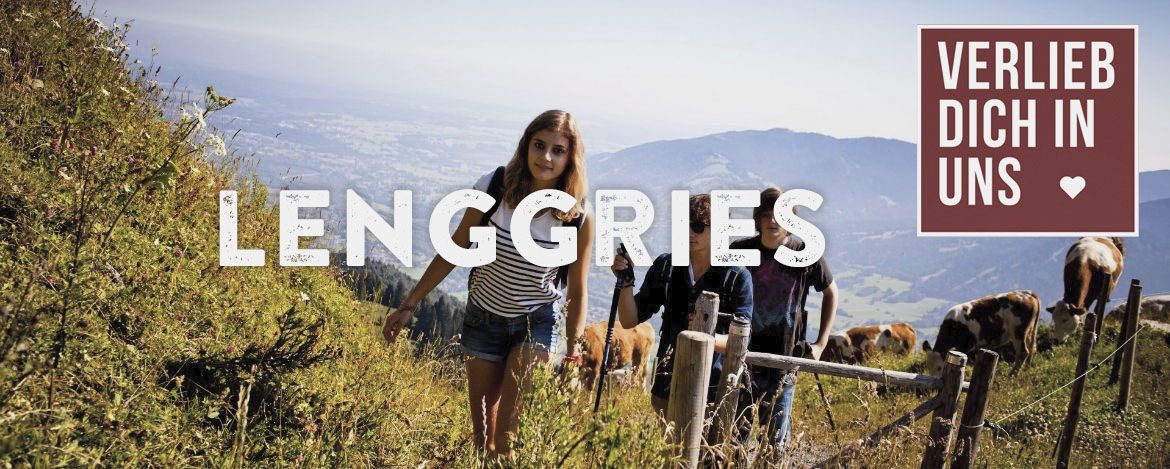 Flache Hügel und junge Personen, die ihren Ausflug im Sommer in den Bergen genießen. Die Beschriftung ist Lenggries und der Hinweis auf das Verlieb dich in uns Angebot befindet sich in der rechten Ecke.
