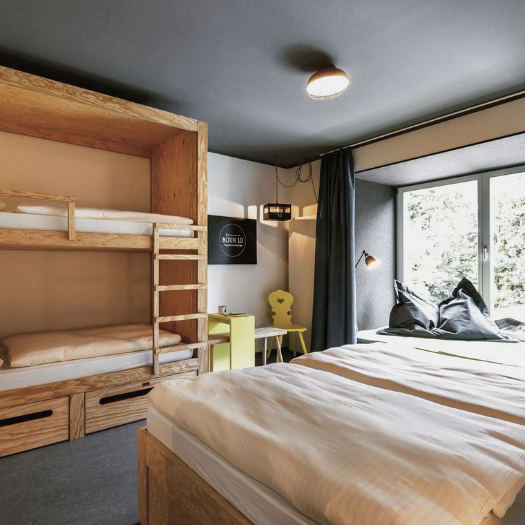 Blick in ein Zimmer der Jugendherberge mopun10 in Garmisch-Partenkirchen mit einem Doppelbett und einem Etagenbett.