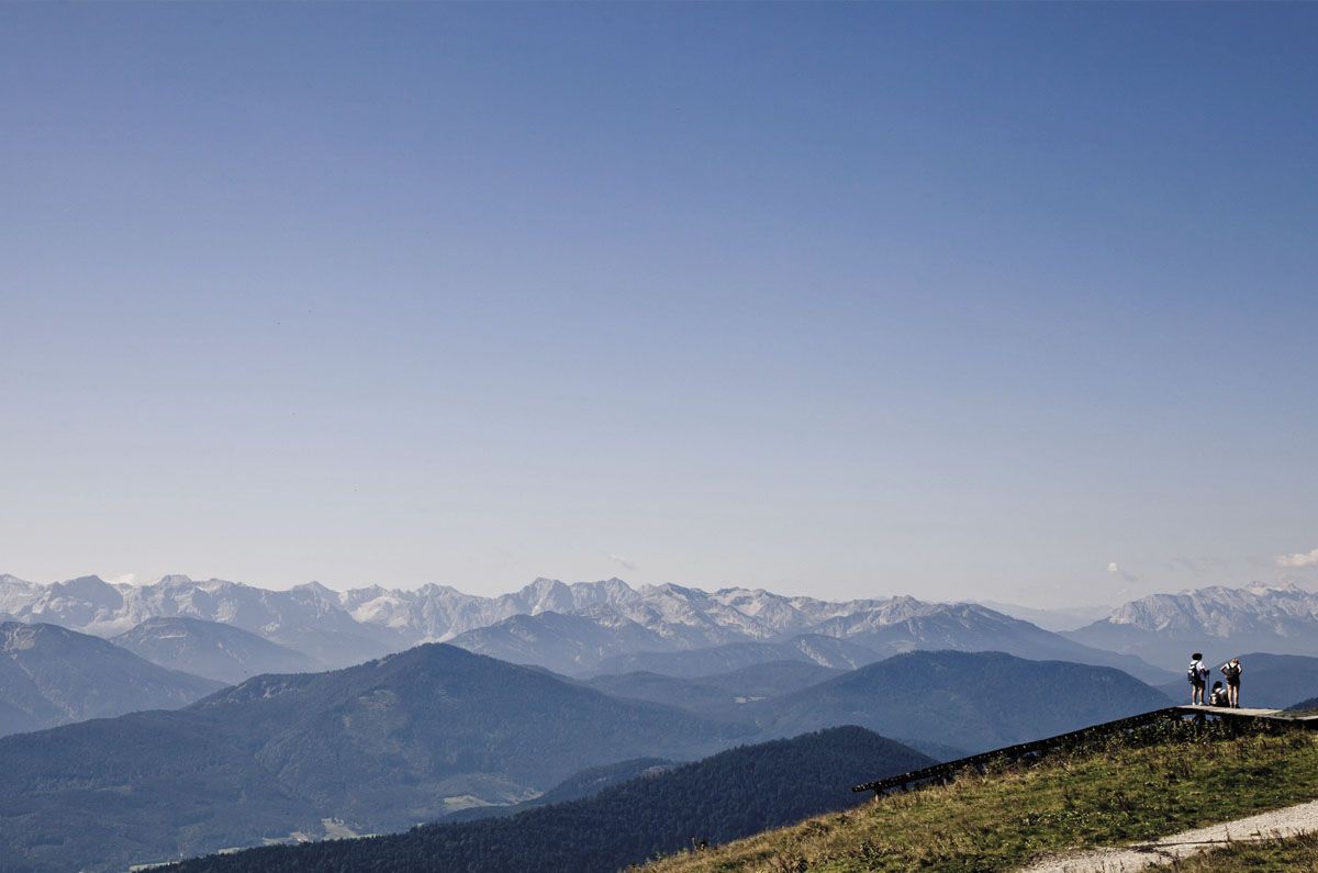 Blick über die Gipfel der Alpen. Das Foto wird zu zwei Drittel von einem wolkenlosen blauen Himmel dominiert. Ganz unten rechts sieht man auf dem Foto eine kleine Gruppe von Menschen.