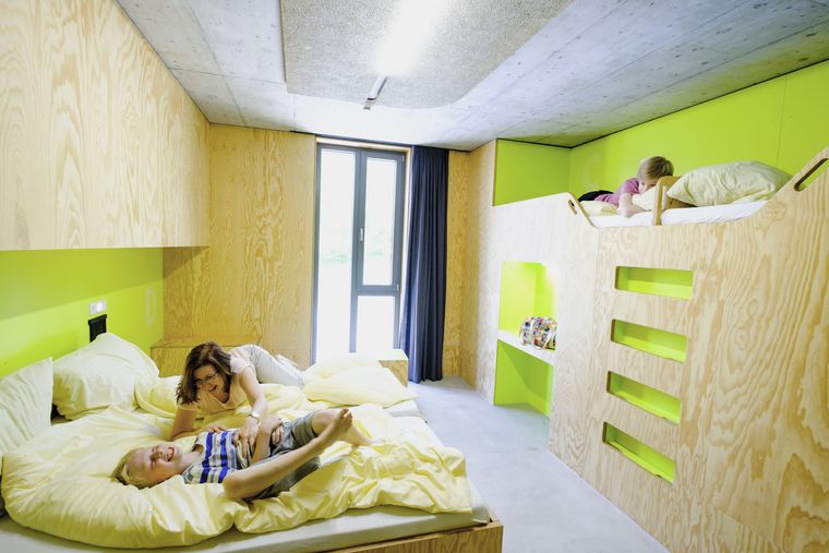 Ein helles Zimmer mit hellgrünen Wänden in der Jugendherberge Bayreuth, in der eine Mutter mit zwei Kindern herumtobt