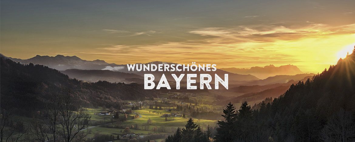 Eine hügelige Landschaft mit Wiesen, Wäldern und Bergen im Sonnenuntergang. Das Foto wird überlagert von dem Text "Wunderschönes Bayern".