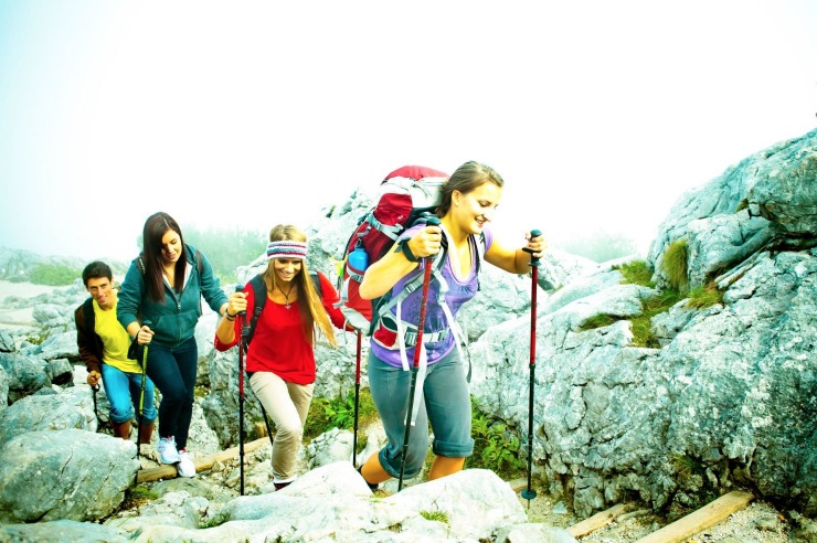 Vier junge Erwachsene beim Bergwandern mit Wanderstöcken und Rucksäcken